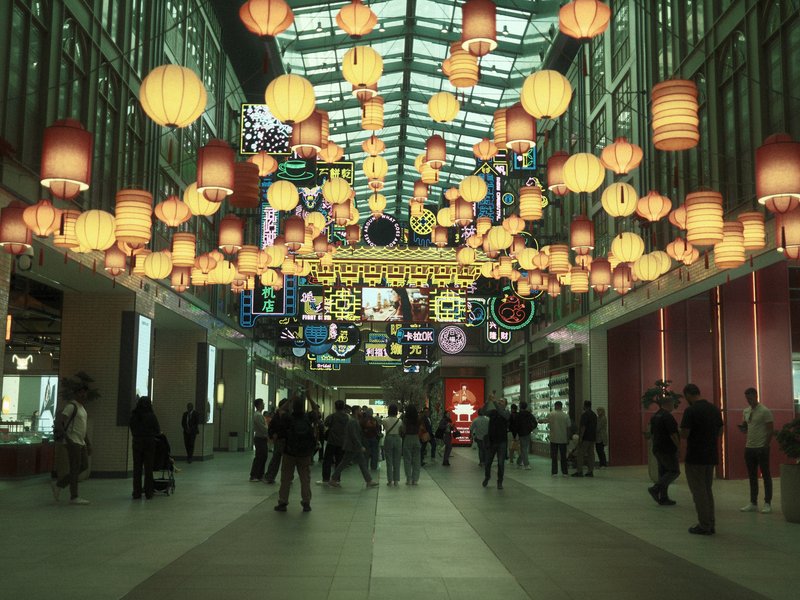 A bustling indoor market with hanging lanterns and people walking beneath them.
