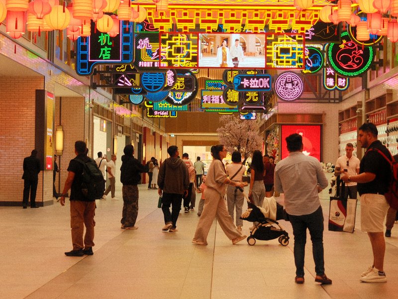 A bustling indoor shopping area filled with colorful neon signs and lanterns, with people walking around.