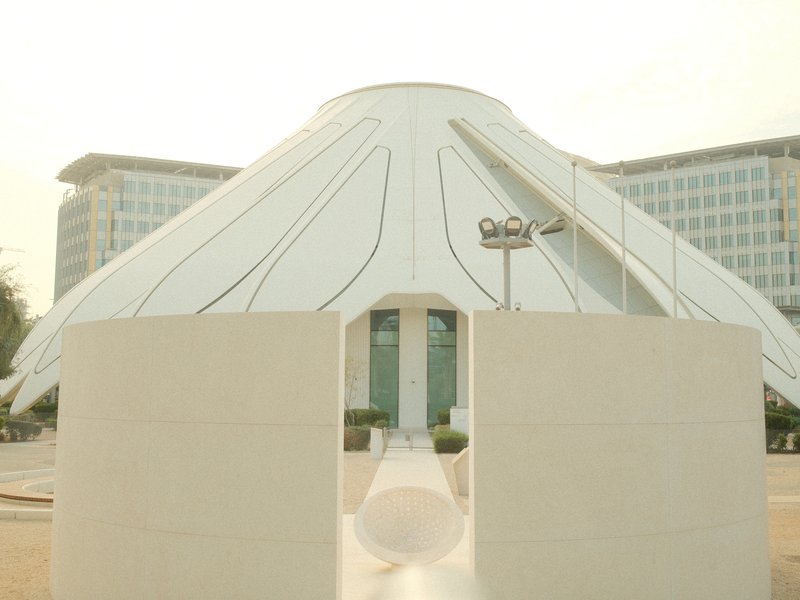 A modern architectural structure with a white canopy resembling a flower, set against a glass building.