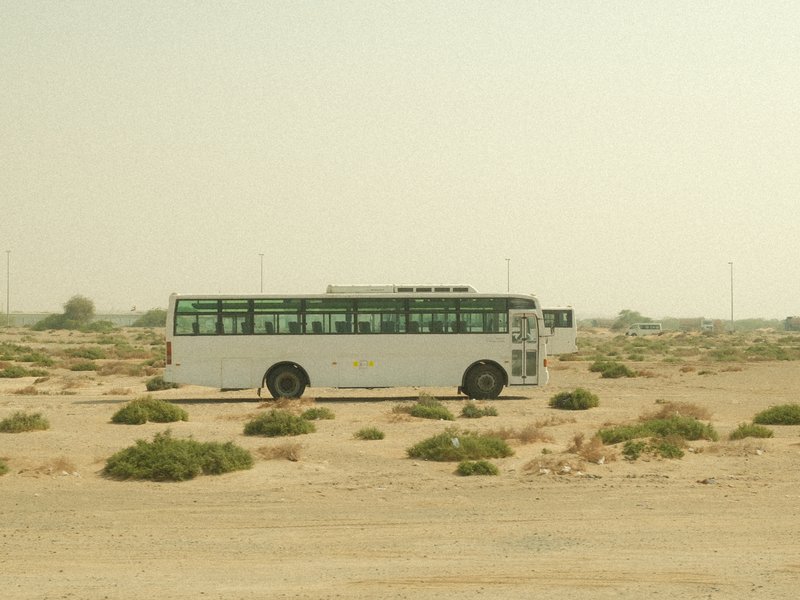 A white bus parked in a barren desert landscape with sparse vegetation under a hazy sky.