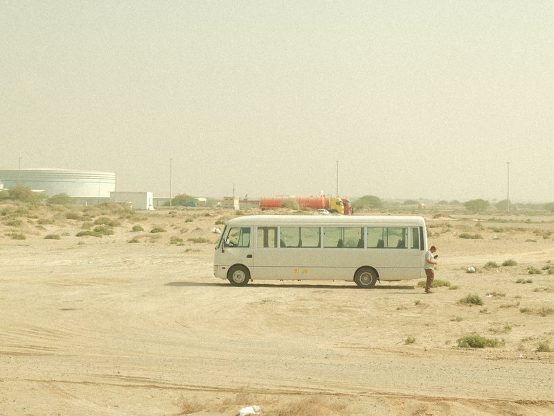 A white bus parked in a dusty, barren landscape under a hazy sky.