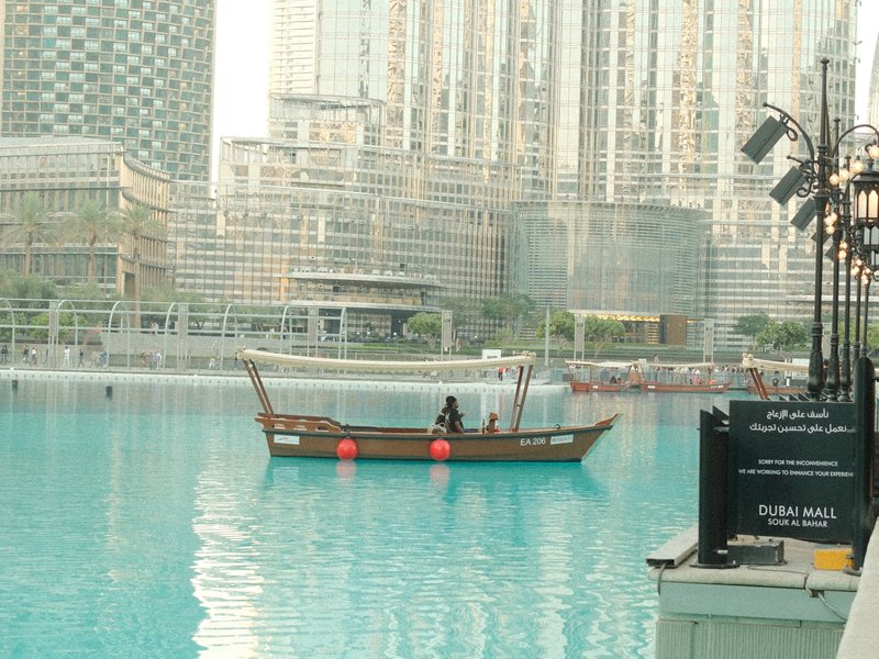 A traditional boat on a turquoise water body with modern skyscrapers in the background.