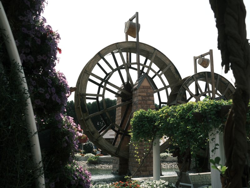 Two large decorative water wheels surrounded by lush greenery and flowers in a garden setting.