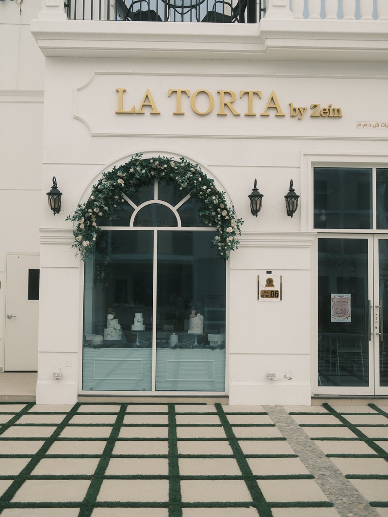 Facade of a bakery named 'La Torta' with decorative greenery and a tiled entrance.