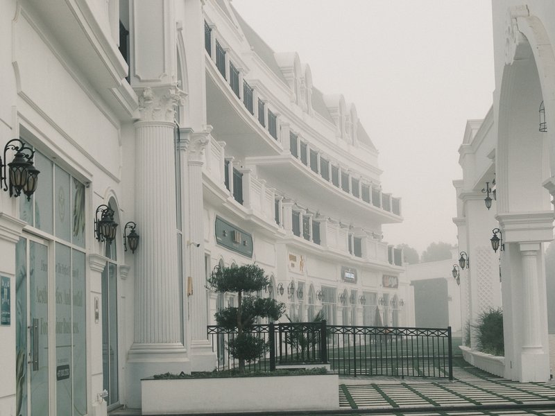 A foggy scene of white colonial-style buildings with a courtyard and decorative ironwork.
