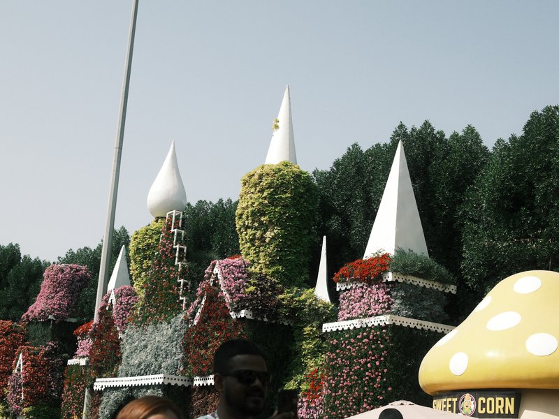 Colorful floral castle structures with spires surrounded by greenery under a clear sky.