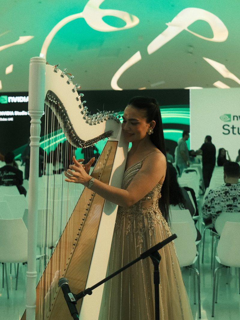 A woman in an elegant dress playing a harp at a modern event with a green-lit background.