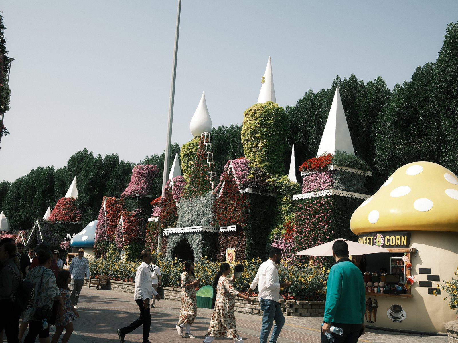 Colorful floral structures resembling castles and mushrooms in a park with people walking.