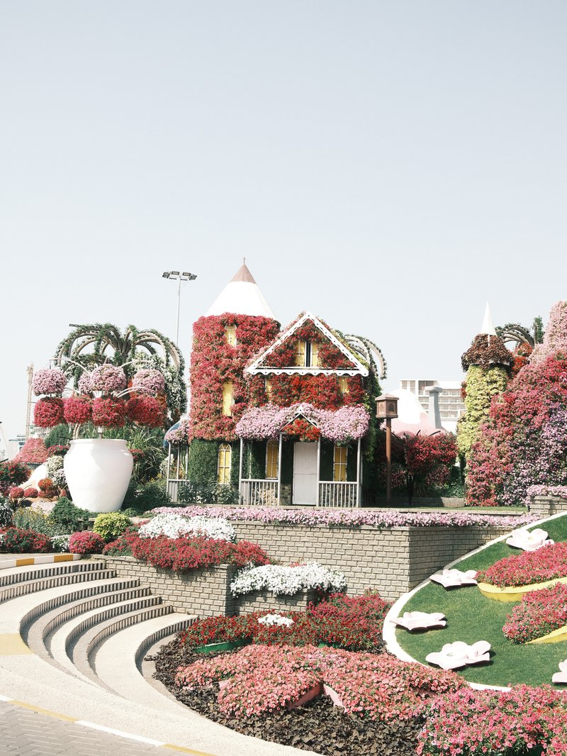 A colorful flower-covered house surrounded by vibrant floral displays and landscaped steps.