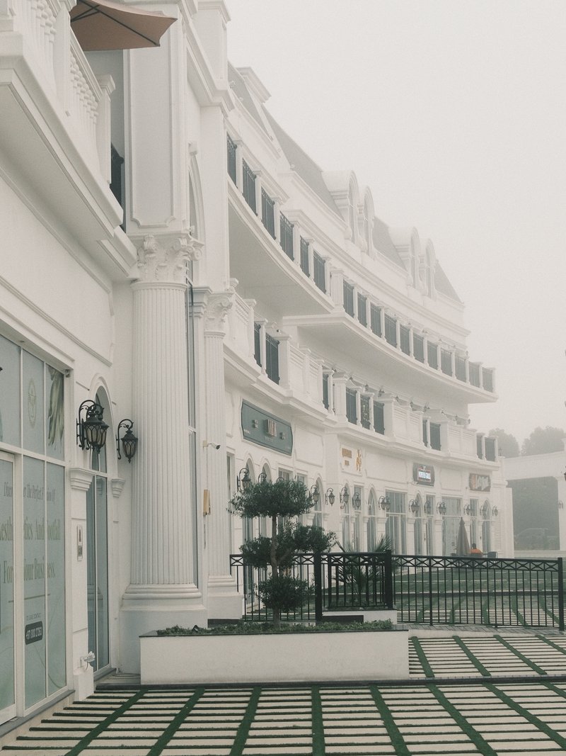 A foggy scene of a white building with columns and a patterned pavement in a quiet setting.