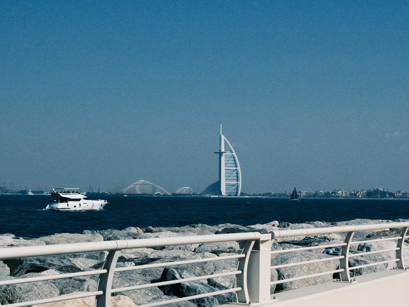 A view of the Burj Al Arab hotel in Dubai with a boat on the water and rocky shoreline in the foreground.