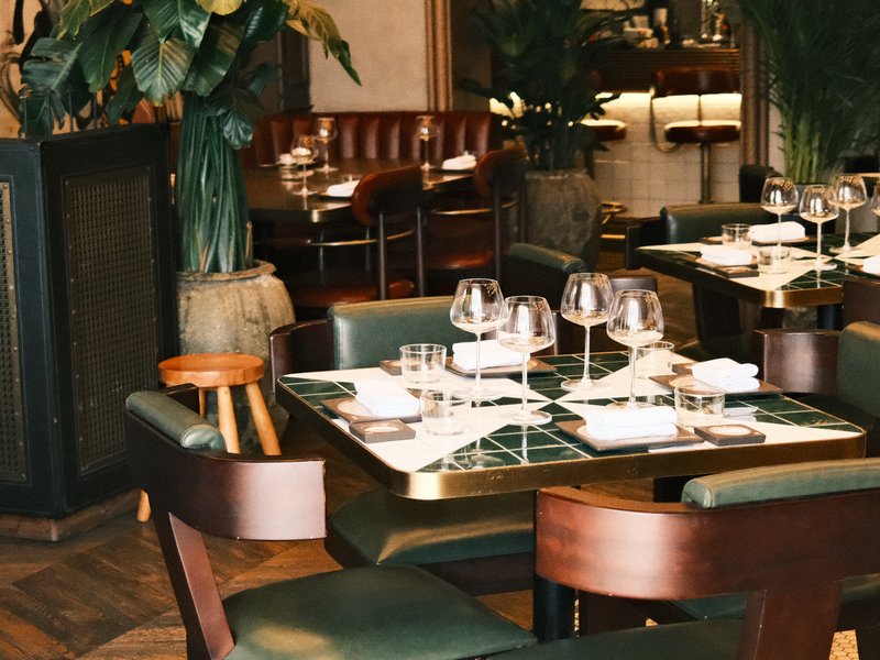 Elegant restaurant interior with tables set for dining, featuring green chairs and glassware.