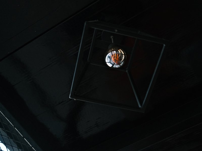 A geometric black light fixture hanging from a dark ceiling, with a bulb reflecting light.