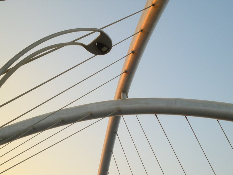 Close-up of a modern bridge structure with cables and a lamp against a clear sky.