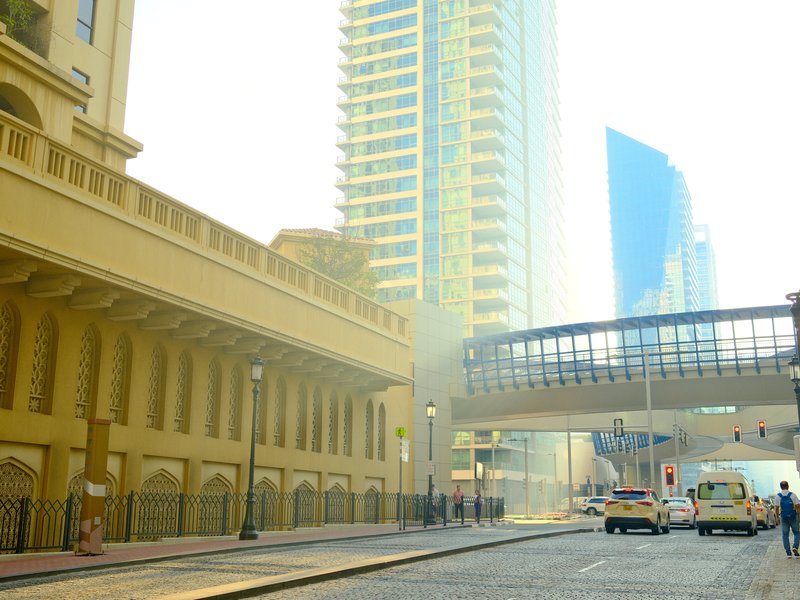 A hazy urban street scene featuring tall buildings and a pedestrian bridge.