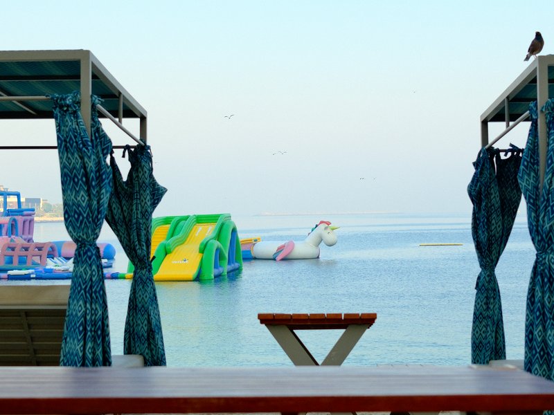 View of colorful inflatable water park structures from a shaded seating area by the water.