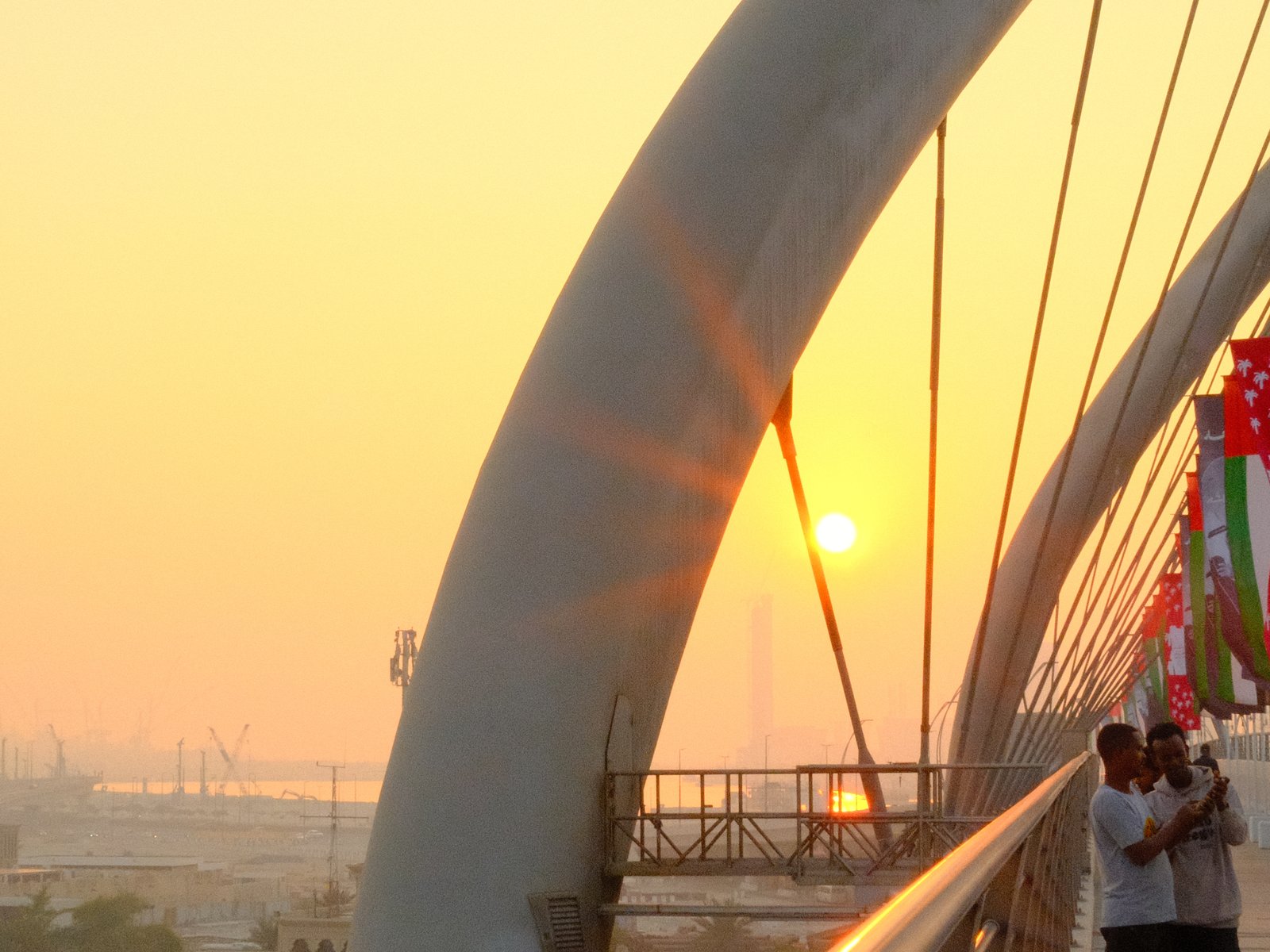 A sunset view from a bridge with silhouettes of people and vibrant colors in the sky.