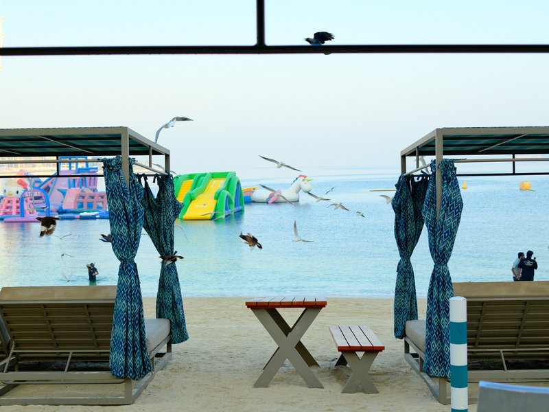 Two beach cabanas facing a water park with inflatable structures and seagulls flying above.