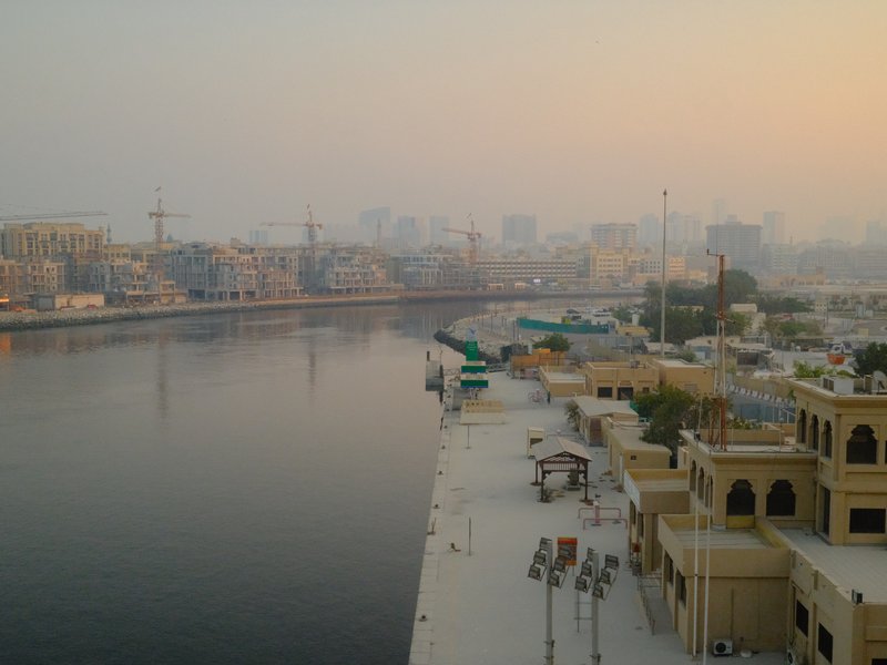 A serene view of a river with city skyline in the background during sunset, featuring buildings and calm water.