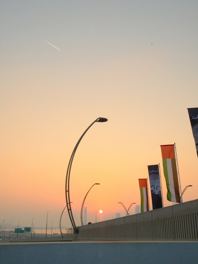 Sunset over a cityscape with streetlights and colorful banners along a bridge.