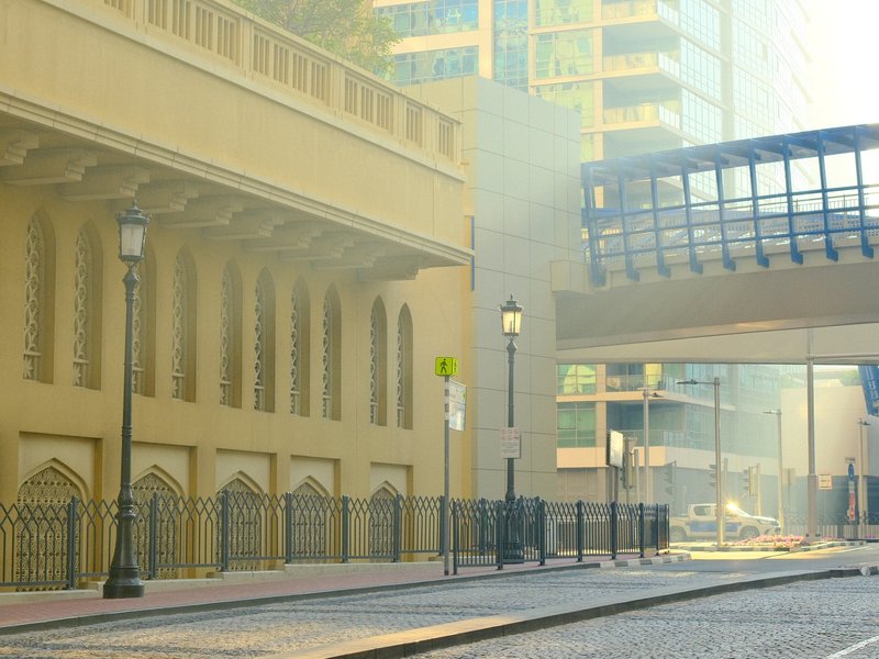 A foggy urban scene with a bridge overhead and a cobblestone street lined with lampposts.