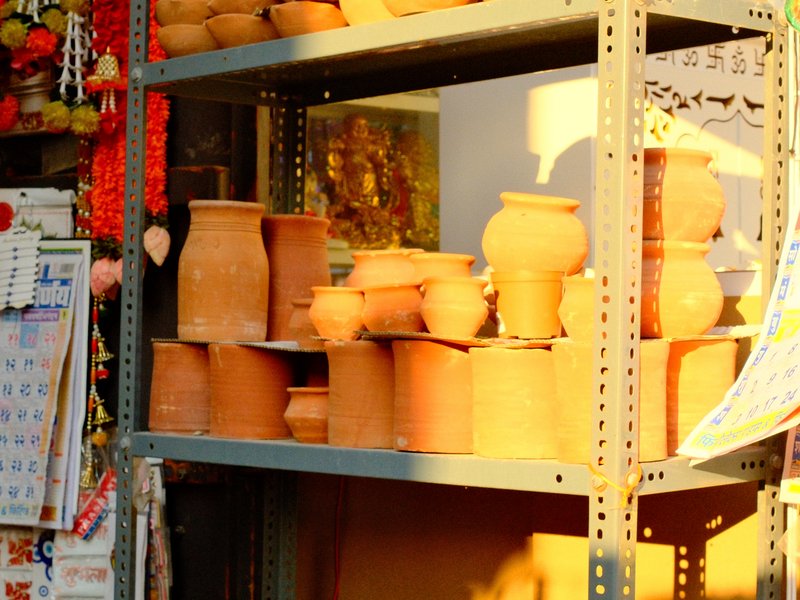 Clay pots and decorative items displayed on a shelf with warm sunlight illuminating the scene.