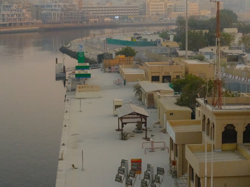 A serene waterfront scene with buildings along a riverbank at dawn, reflecting soft light.