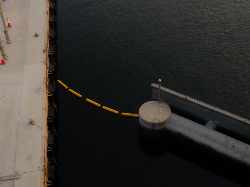 Aerial view of a circular dock extending into dark water with a yellow barrier floating nearby.