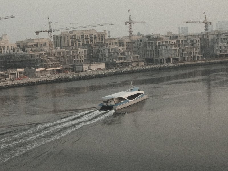A boat gliding through calm water with urban construction in the background.