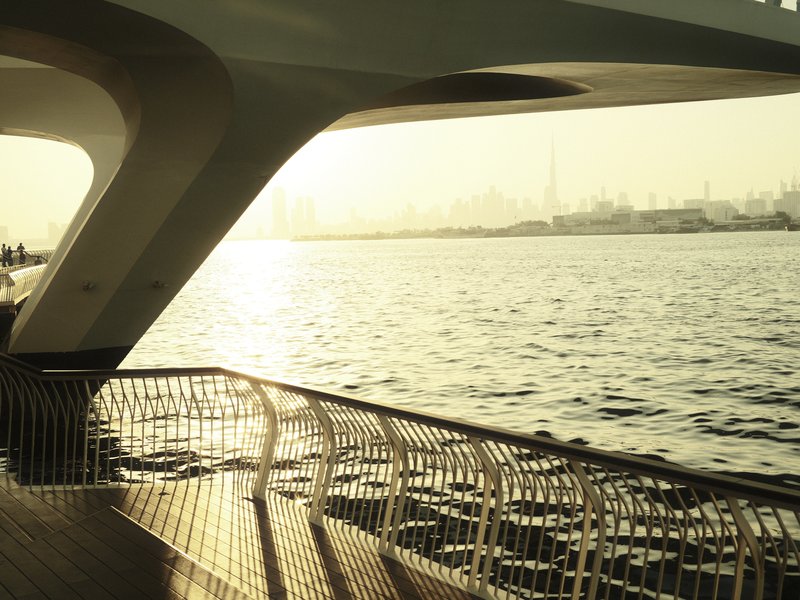 A view of a waterfront with a curved railing and soft sunlight reflecting on the water.