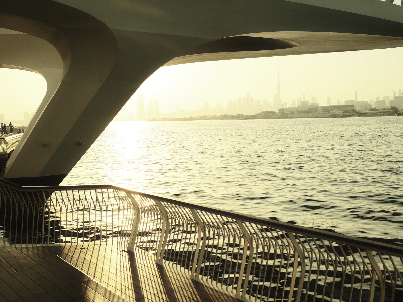 A view of a waterfront with a curved railing and soft sunlight reflecting on the water.