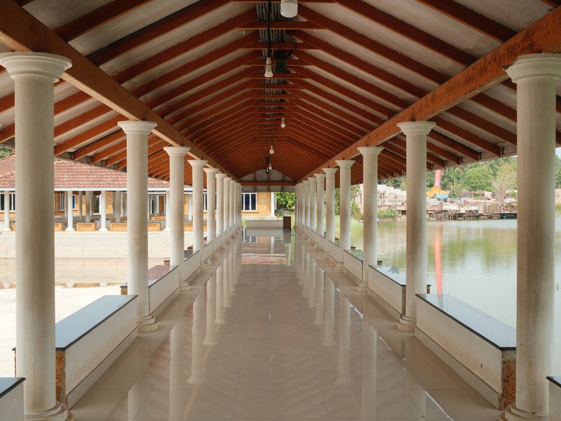 A long corridor with wooden beams and columns, leading to a serene water view.