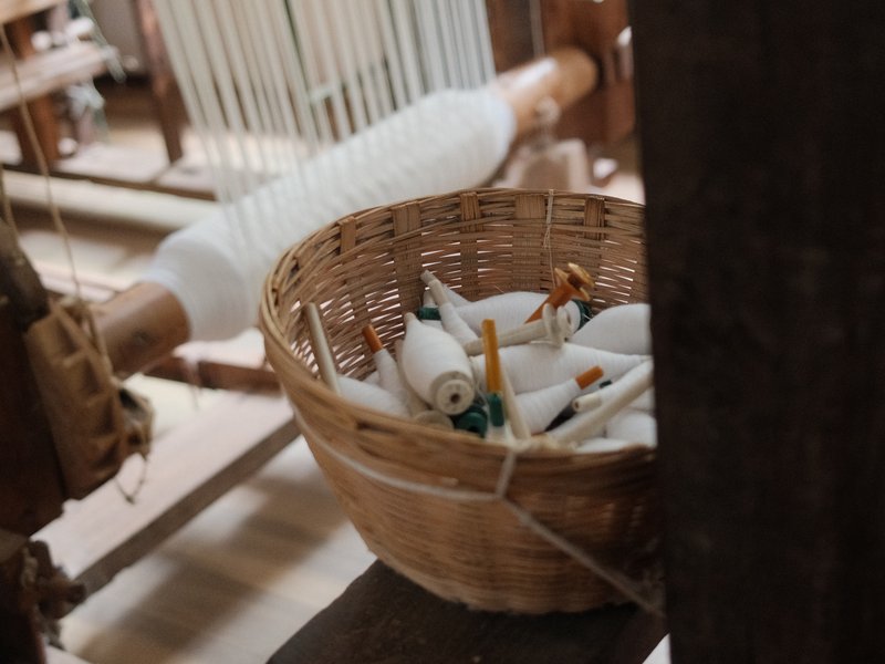 A woven basket filled with colorful spools of thread, set in a weaving workshop.