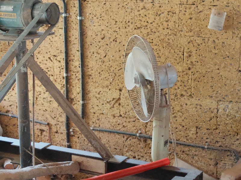 A close-up of a fan and machinery in a rustic indoor setting with textured walls.