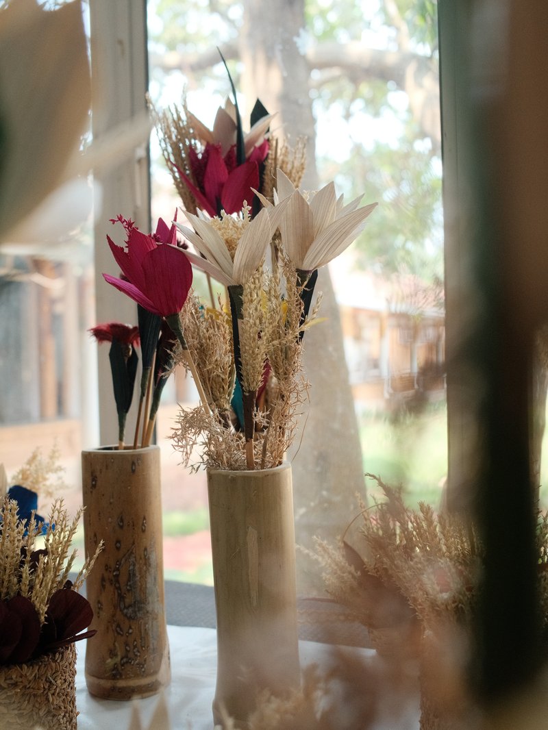 A close-up of decorative dried flowers in vases by a window with soft natural light filtering through.