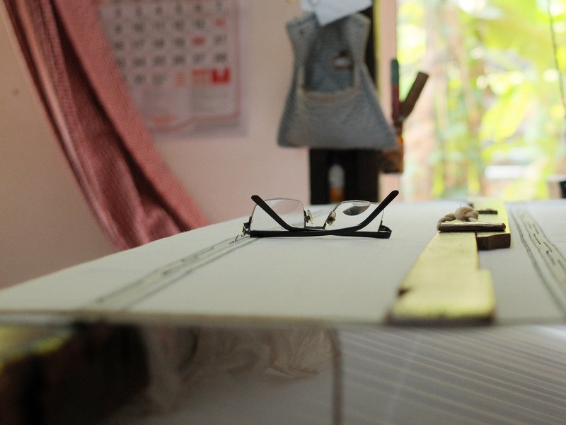 A close-up view of a pair of glasses resting on a table with a blurred background of a room.