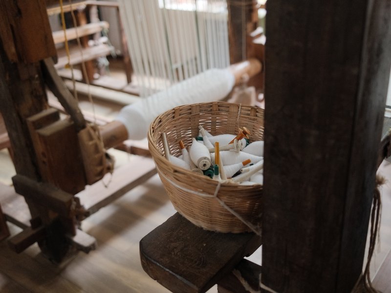 A close-up view of a weaving loom with a basket of colorful spools and tools nearby.