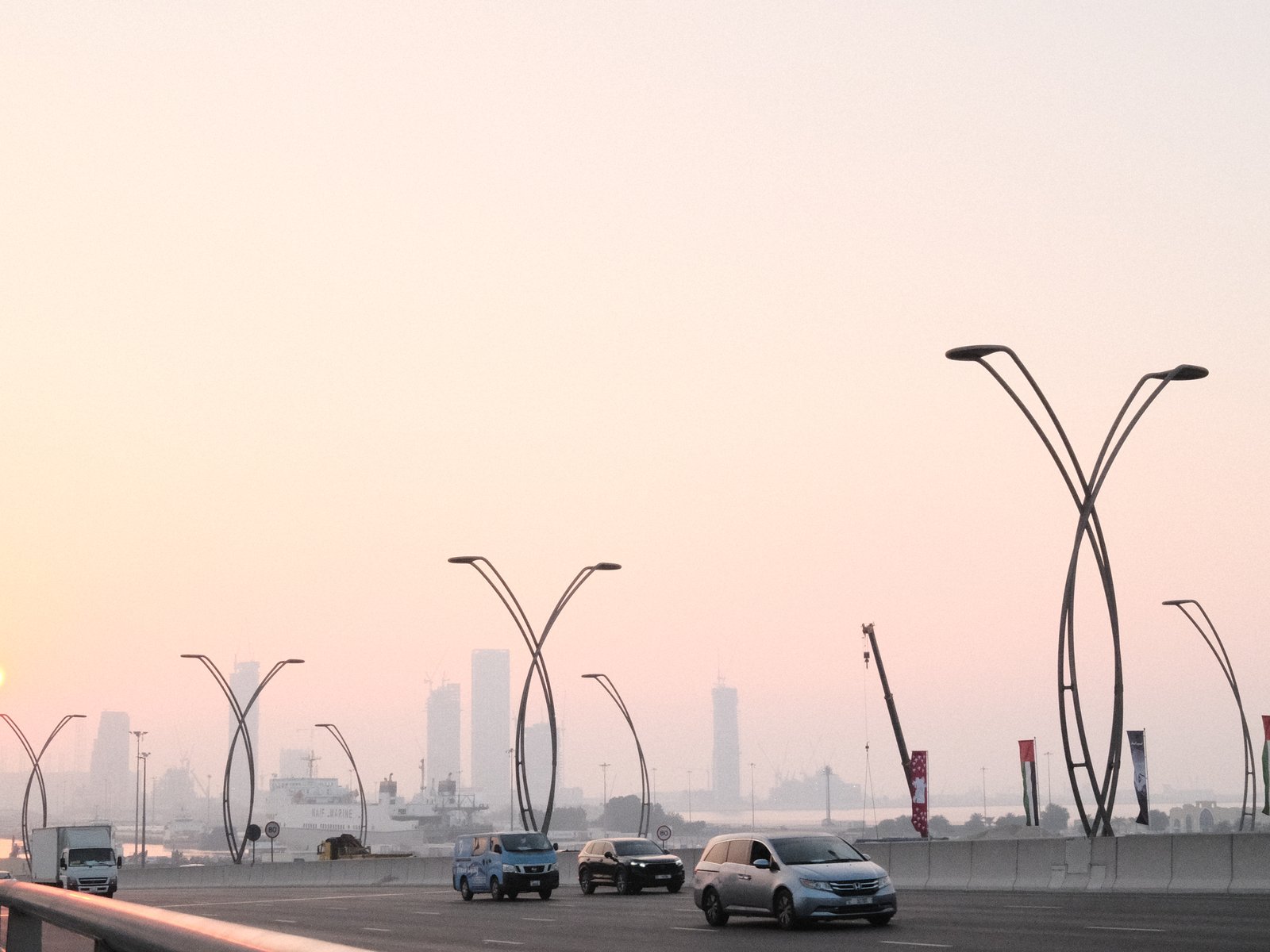 A cityscape at dusk featuring modern street lamps and vehicles on a bridge with a hazy skyline.