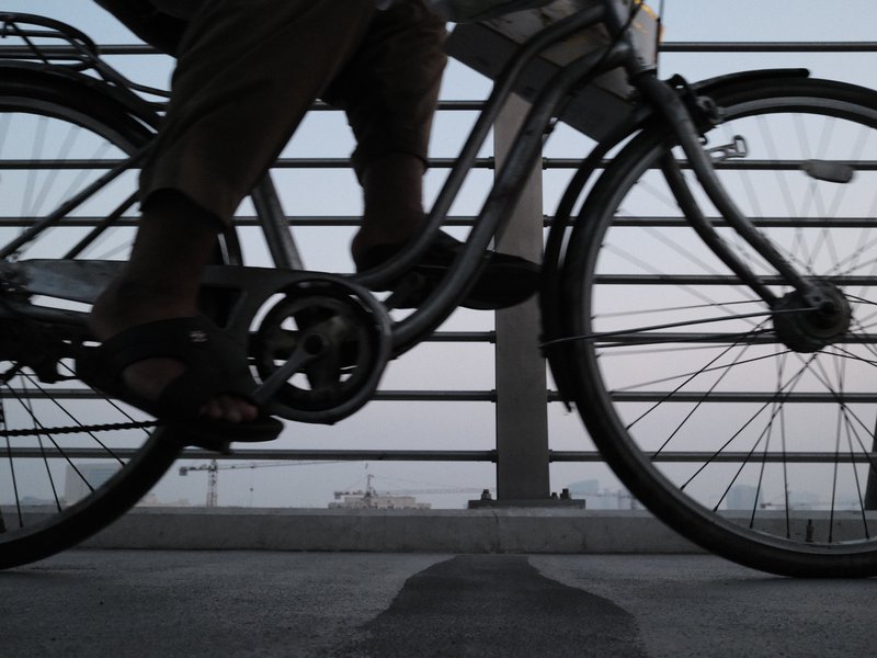 Close-up of a person riding a bicycle on a bridge, with a focus on the bike's pedals and the rider's legs.
