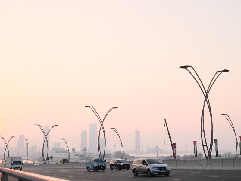 A hazy urban skyline at dusk with modern street lamps and cars on a bridge.