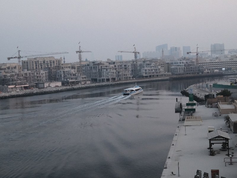 A boat navigating a river surrounded by construction sites and a hazy skyline.
