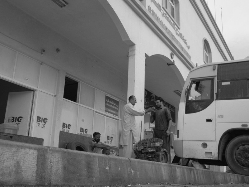 A busy urban scene with people interacting near a bus and a building entrance.