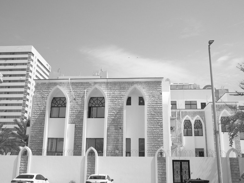 Black and white photo of a historic building with arched windows and modern buildings in the background.