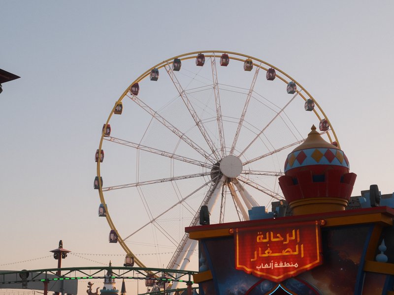 Ferris wheel against a sunset sky with a colorful structure in the foreground.