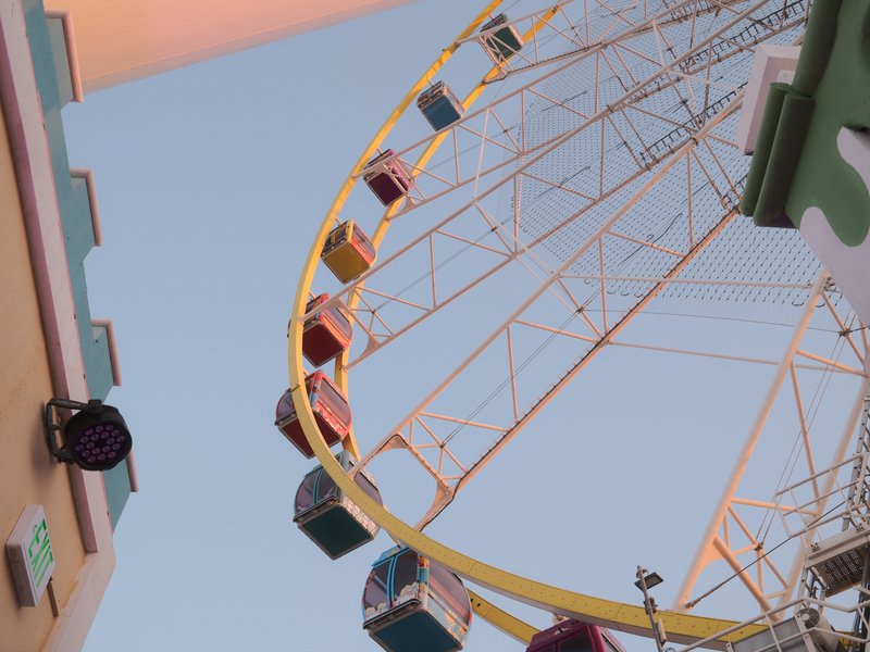 A colorful ferris wheel against a clear sky, viewed from below with buildings on either side.