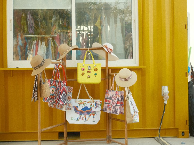 Colorful bags and hats displayed on a wooden rack in front of a yellow container.
