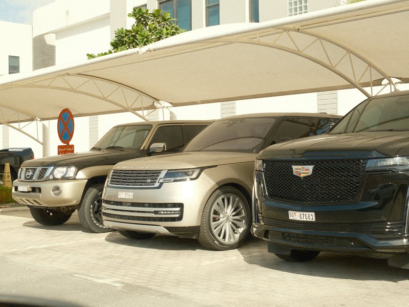 Three luxury SUVs parked under a canopy in a modern urban setting.