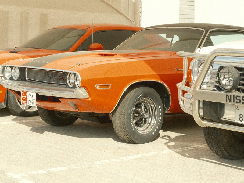 Three classic cars parked side by side, featuring an orange muscle car in the foreground.