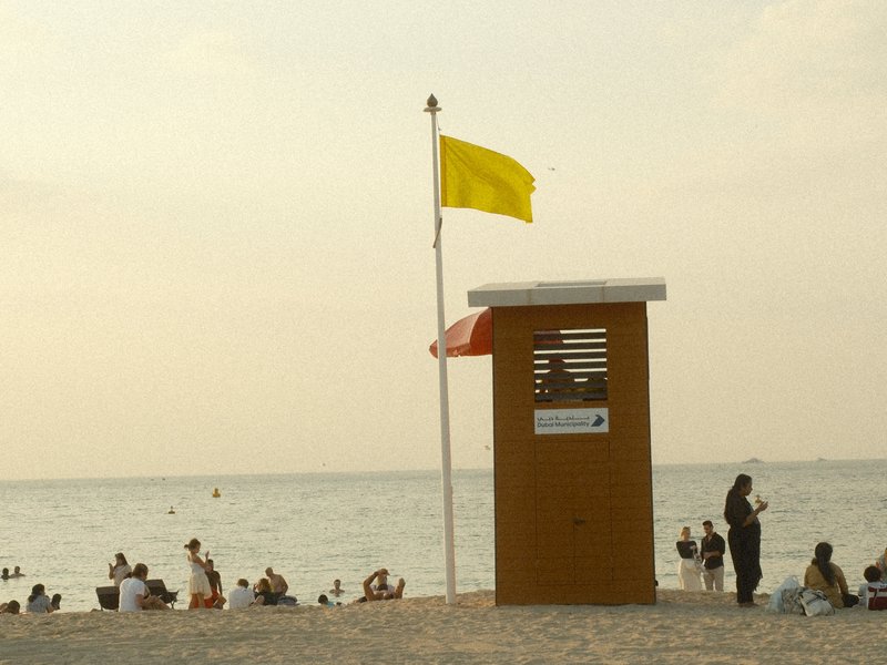 Lifeguard station on a beach with yellow and red flags, people swimming in the sea.