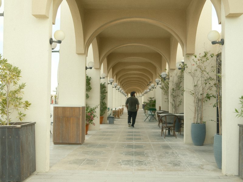A person walking down a corridor lined with arches and potted plants.